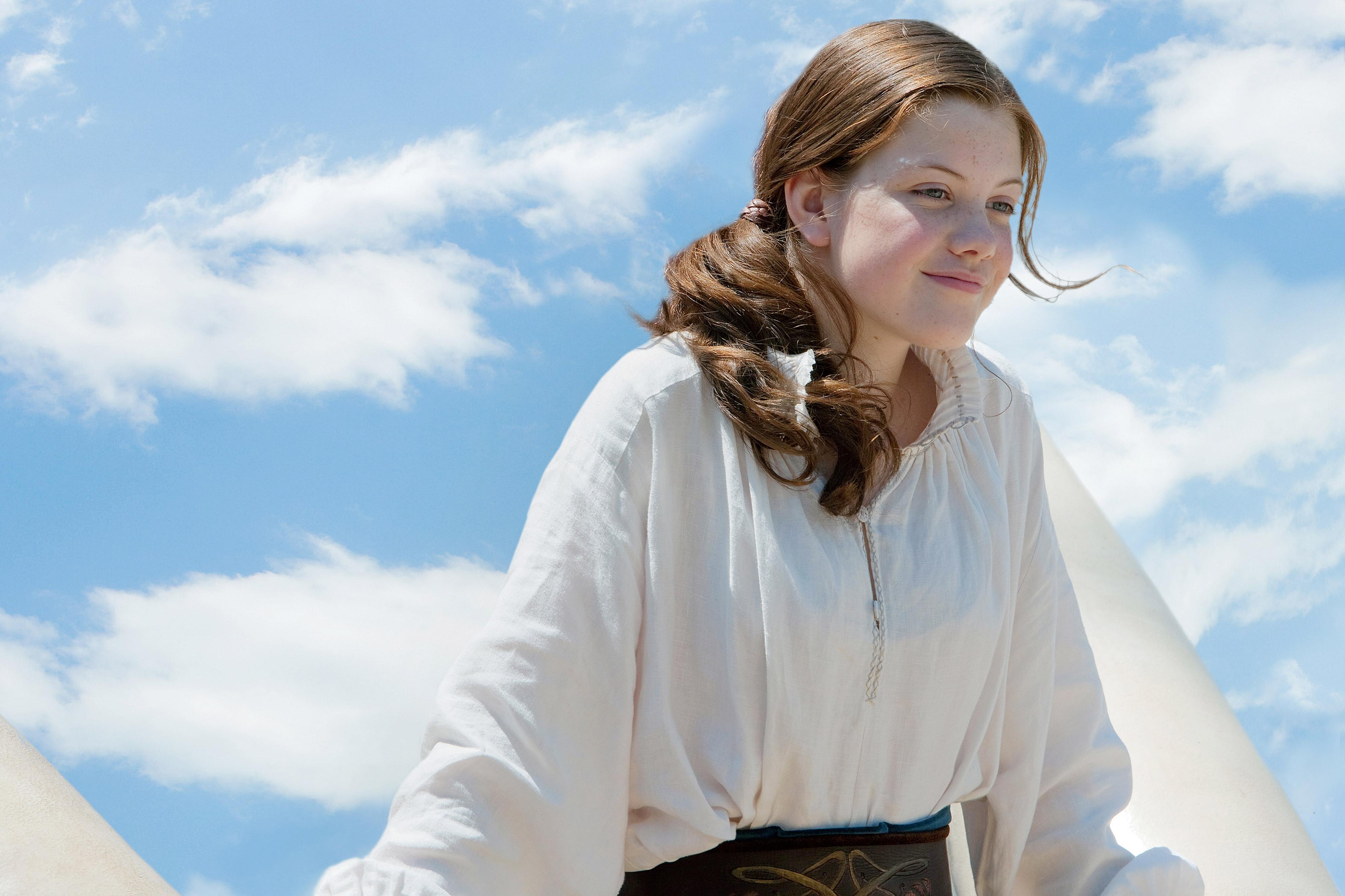 Georgie Henley is playing lucy. She is looking over the side of the Dawn Treader with a partially cloudy blue sky in the background.