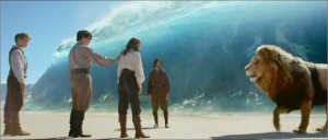 Eustace stands several feet behind Edmund who stands closely behind Lucy. They are on the beach at the Word's End with a 20 ft wave leading into Aslan's Country. Aslan talks to lucy and Caspian stands back in the distance.