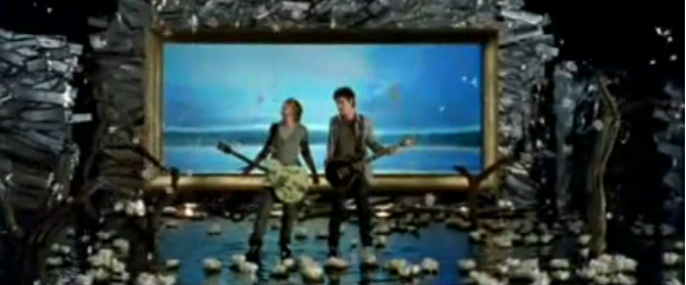 The Italian band Sonohra stands in a pool of water with lilies on top. Behind them a giant paining shows clips from The Voyage of the Dawn Treader Movie.